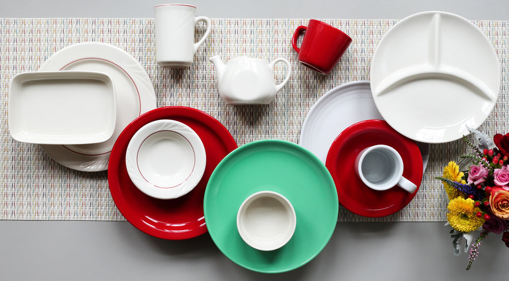 Colorful tableware including plates, cups, and a teapot on a textured surface.